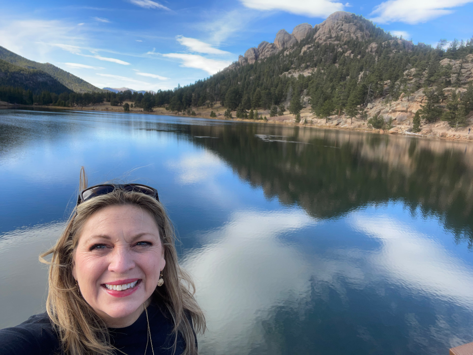 Phalynn smiling in front of a mountain lake with rocky peaks behind her
